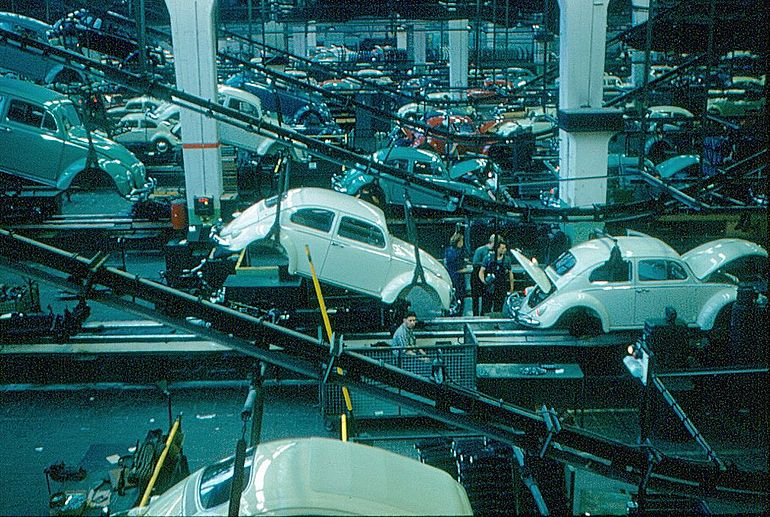 Automobilproduktion 1960: Innenansicht des Volkswagen-Werks. Karosserien werden von einer &Uuml;berkopf‑F&ouml;rderanlage auf Fahrgestelle abgesenkt.