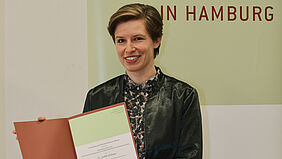 Die Preistr&auml;gerin Judith Niehaus pr&auml;sentiert l&auml;chelnd die Urkunde f&uuml;r den Elise-Reimarus-Preis 2022.
