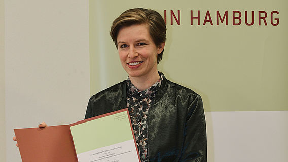 Die Preisträgerin Judith Niehaus präsentiert lächelnd die Urkunde für den Elise-Reimarus-Preis 2022.