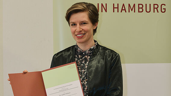 Die Preistr&auml;gerin Judith Niehaus pr&auml;sentiert l&auml;chelnd die Urkunde f&uuml;r den Elise-Reimarus-Preis 2022.