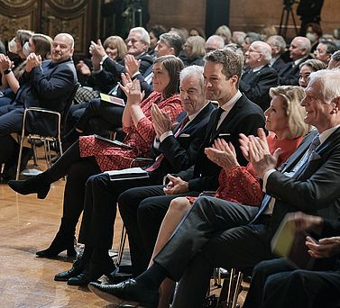 Der Preistr&auml;ger Prof. Dr. Dr. Fabian Theis inmitten von applaudierendem Publikum. Er sitzt in der vordersten Reihe neben Wissenschaftssenatorin Katharina Fegebank, Prof. Dr. Edwin J. Kreuzer und Eva-Maria Greve.