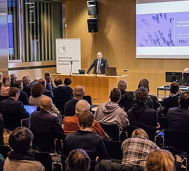 Prof. Dr. Ansgar Lohse steht hinter dem Rednerpult und spricht zum Publikum. Hinter ihm auf einer Leinwand ist der Titel des Vortrags von Prof. Dr. Dr. h. c. Lothar Wieler zu sehen: &bdquo;Future challanges of AMR &ndash; the ongoing pandemic&ldquo;.