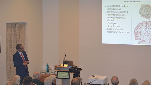 ein Gastsprecher trägt vor einem Publikum in einem großen Saal einen Vortrag vor