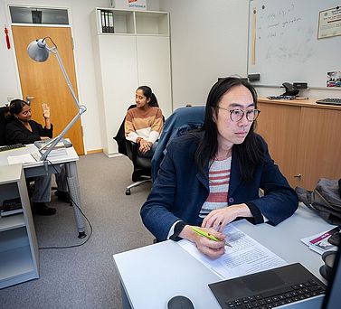 Charles Li gemeinsam mit Forscherinnen im B&uuml;ro