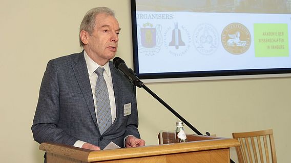 Der ehemalige Akademiepr&auml;sident Prof. Kreuzer auf der 18. "Baltic Conference on Intellectual Cooperation" am Rednerpult vor der Leinwand mit den Logos der veranstaltenden Wissenschaftsakademien Lettland, Litauen, Estland, Finnland und Hamburg.