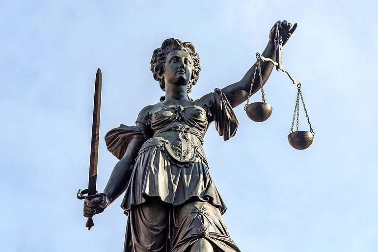 Die Bronzestatue der römischen Göttin der Gerechtigkeit Justitia vor einem blauen Himmel.