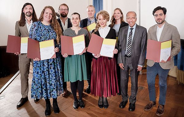 Die Young Academy Fellows bei der feierlichen Aufnahme am 16. Oktober 2025 mit Akademiepr&auml;sident Prof. Dr. Mojib Latif (von links): Dr. Pierre Sfendules, Dr. Katrin Kleemann, Dr. Jan S. Krause, Dr. Amra Jahic, Dr. Fabien Schultz, Dr. Carolin Gluchowski, Dr. Clara-Auguste S&uuml;&szlig; und Dr. Andr&eacute;s L&oacute;pez Rivera. Nicht auf dem Bild zu sehen ist Dr. Alica Repenning.