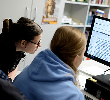 Zwei Wissenschaftlerinnen sitzen vor einem Computerbildschirm und betrachten eine digitalisierte historische Quelle.