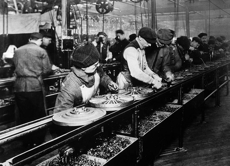 Automobilproduktion 1913: Arbeiter auf einem der ersten Flie&szlig;b&auml;nder montieren Schwungr&auml;der f&uuml;r Ford-Autos.