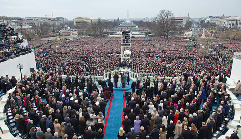 Die Amtseinf&uuml;hrung von Donald Trump vor dem Kapitol in Washington D.C aus der Sicht des US-Pr&auml;sidialamtes. Um ihn herum stehen zahlreiche Politiker und G&auml;ste, auch der Platz vor dem Kapitol ist gef&uuml;llt. Der Himmel ist bew&ouml;lkt.