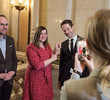 Preistr&auml;ger Prof. Dr. Dr. Fabian Theis und Katharina Fegebank werden mit einem Smartphone fotografiert, w&auml;hrend Katharina Fegebank mit ihren Zeigefingern auf Fabian Theis zeigt. Links neben ihnen steht Christoph Bock.