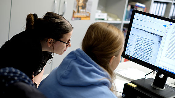 Zwei Wissenschaftlerinnen sitzen vor einem Computerbildschirm und betrachten eine digitalisierte historische Quelle.