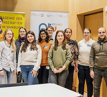 Ein Gruppenfoto von an der Tagung teilnehmenden Doktorand:innen. Hinter ihnen ist das Banner der Akademie der Wissenschaften in Hamburg und des DFG-Graduiertenkollegs 2719 zu sehen.