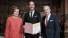 Der Preistr&auml;ger Prof. Dr. Dr. Fabian Theis h&auml;lt die Urkunde f&uuml;r den Hamburger Wissenschaftspreis in den H&auml;nden. Theis steht zwischen der Stifterin Eva-Maria Greve und Akademiepr&auml;sident Prof. Dr. Edwin J. Kreuzer im Hamburger Rathaus.
