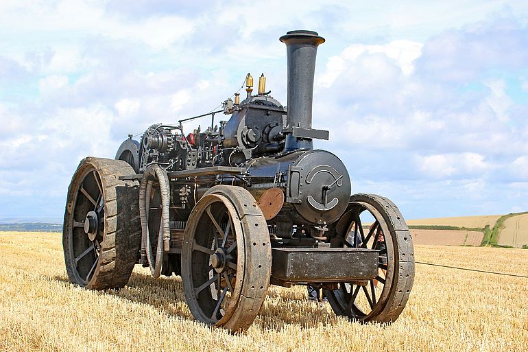Ein schwarzer Dampftraktor aus dem sp&auml;ten 19. Jahrhundert auf einem Stoppelfeld.